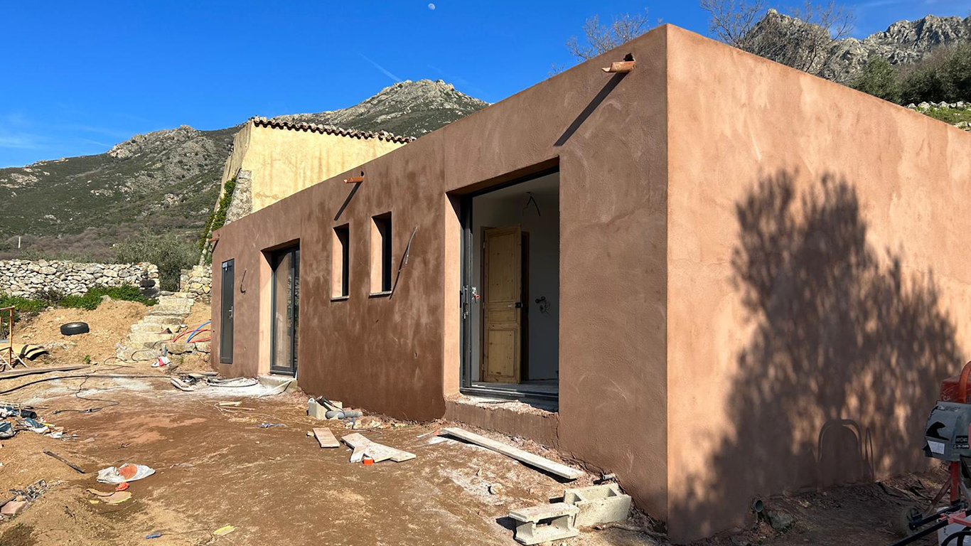 Façade finie avec enduit couleur terre, menuiseries installées et vue sur les montagnes de Balagne.