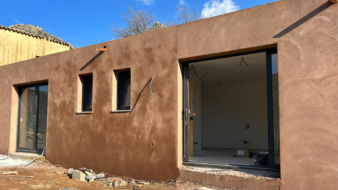 Détail des ouvertures et des menuiseries noires sur l'enduit de façade.