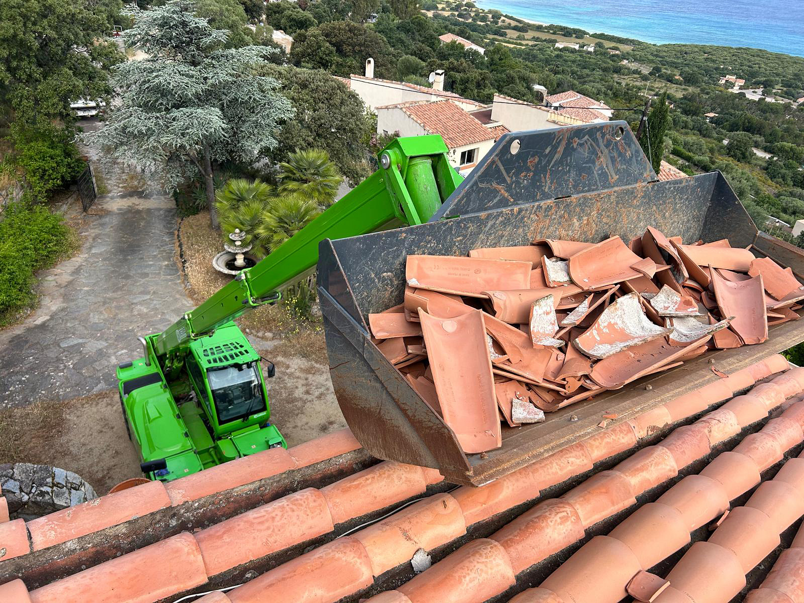 Évacuation des gravats et anciennes tuiles à l'aide de la benne Merlo, avec vue sur la mer.
